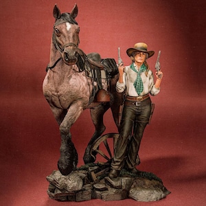 May include: A detailed figurine of a woman in Western attire, holding two pistols, stands beside a saddled horse. The woman wears a hat, scarf, and dark pants. The horse is a dappled gray color. The base features rocks and a broken wagon wheel.