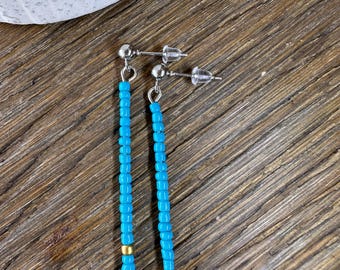 May include: A pair of long, turquoise blue beaded earrings with gold accents. The earrings are made with small, round beads and have a simple, elegant design.