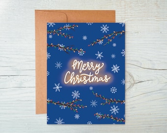 May include: A Christmas card with a blue background, decorated with white snowflakes and branches with colourful lights. The words "Merry Christmas" are written in a glowing, cursive font. The card is accompanied by a brown envelope.