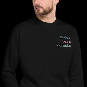 May include: Black sweatshirt with the words "code; test commit" in a teal, pink, and blue font. The sweatshirt is a solid black color and has a crew neck.