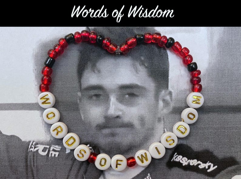 May include: A red and black beaded bracelet with white beads that spell out "WORDS OF WISDOM".