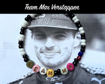 May include: Black and white beaded bracelet with the word "TEAM" and the letter "V" in gold lettering. The bracelet is in front of a photo of a man wearing a black racing cap.