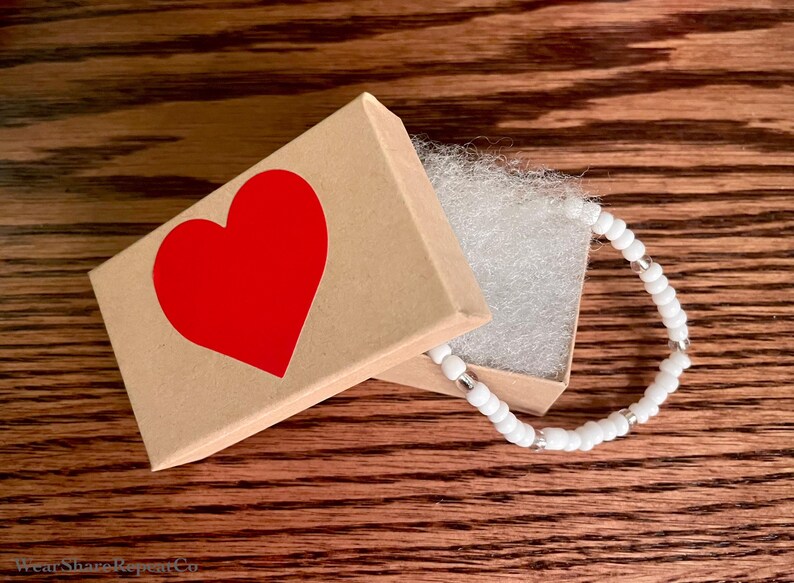 May include: A white beaded bracelet with silver accents in a small brown box with a red heart on the lid.