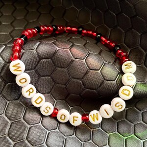 May include: Red and black beaded bracelet with white beads spelling out "WORDS OF WISDOM".