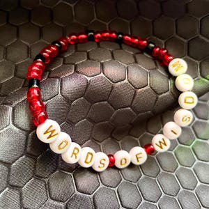 May include: A red and black beaded bracelet with white beads that spell out "WORDS OF WISDOM".