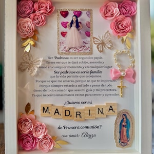 May include: A white frame with a pink and gold floral design. The frame includes a photo of a young girl in a pink dress, a small image of the Virgin Mary, and a message written in Spanish. The message reads: "Ser Padrinos es ser segundos papás. Es ese ser que te dará cobijo, asesoría y amor en cualquier momento y en cualquier lugar Ser padrinos es ser la familia que la vida permite que escojamos. Porque se que me amaras, porque se que te importare, Porque siempre estarás a mi lado a pesar de todo deseo de todo corazón que seas mi guía y mi protectora. Ya que necesito unas manos extras para crecer y aprender. ¿Quieres ser mi M. A. D. R. I. N. A. de Primera comunión? con amor: Aleyza"