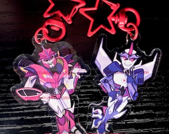 May include: Two acrylic keychains with cartoon robot characters. One is pink and white, the other is blue and white. Both have red star-shaped clasps. The text "TFP KEYCHAINS" is at the bottom.