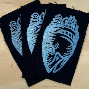May include: Three rectangular black fabric patches featuring a light blue screen-printed graphic of a stylized anatomical heart. The design displays intricate line work and shading, with each patch showing the same heart illustration in a vertical orientation.