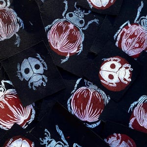 Op de afbeelding: Een verzameling zwarte stoffen patches met insectenillustraties. De insecten zijn afgebeeld in rood, wit en blauw, met ingewikkelde details. De patches zijn verspreid, waardoor een visueel interessant patroon ontstaat.