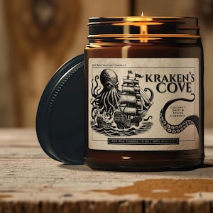 May include: A brown glass jar candle with a black lid. The label features a black and white illustration of an octopus attacking a ship, with the text "KRAKEN'S COVE". The candle is 9 oz and made of soy wax.