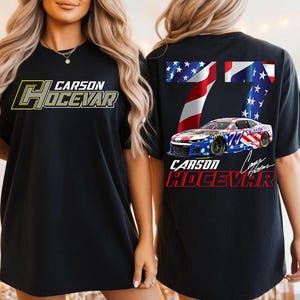 Op de afbeelding: Zwart T-shirt met de tekst "CARSON HOCEVAR" in geel en grijs op de voorkant. De achterkant van het shirt heeft een raceauto-ontwerp met het nummer 77 en de tekst "CARSON HOCEVAR" in rood en wit.
