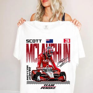 May include: White t-shirt featuring a graphic of an IndyCar driver in a red racing suit and helmet. The shirt includes the driver's name, "Scott McLaughlin," the number "3," and the words "IndyCar Driver" and "Team Penske."