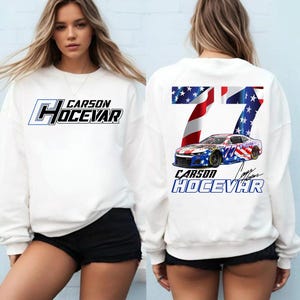 May include: White sweatshirt featuring the text "Carson Hocevar" in blue and black. The back displays a racing car graphic with the number 77, and the driver's name. The design incorporates American flag elements.