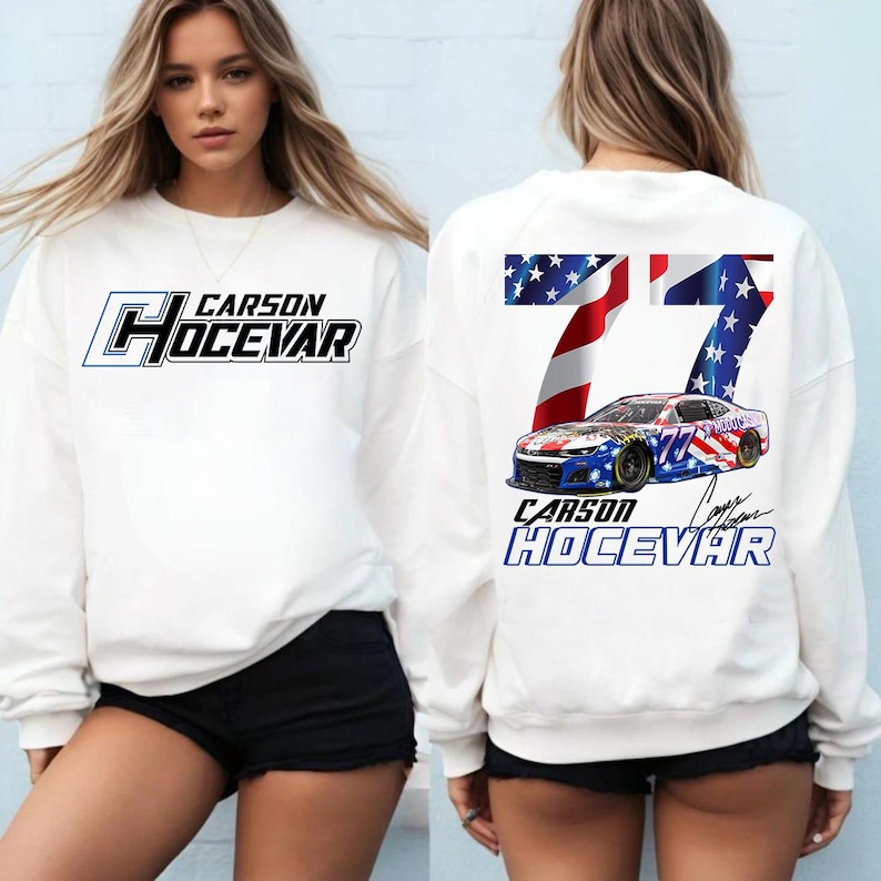 Op de afbeelding: Witte sweatshirt met de tekst "Carson Hocevar" in blauw en zwart. De achterkant toont een raceauto-afbeelding met nummer 77 en de naam van de coureur. Het ontwerp bevat elementen van de Amerikaanse vlag.