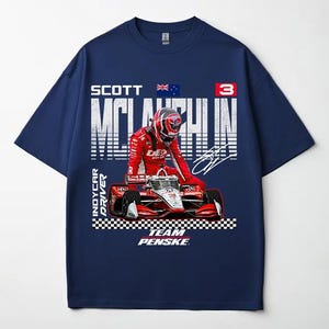 May include: Navy blue t-shirt featuring a graphic of a race car and driver in a red racing suit. The shirt includes the text "SCOTT McLAUGHLIN" and "TEAM PENSKE". The Australian flag is also visible.