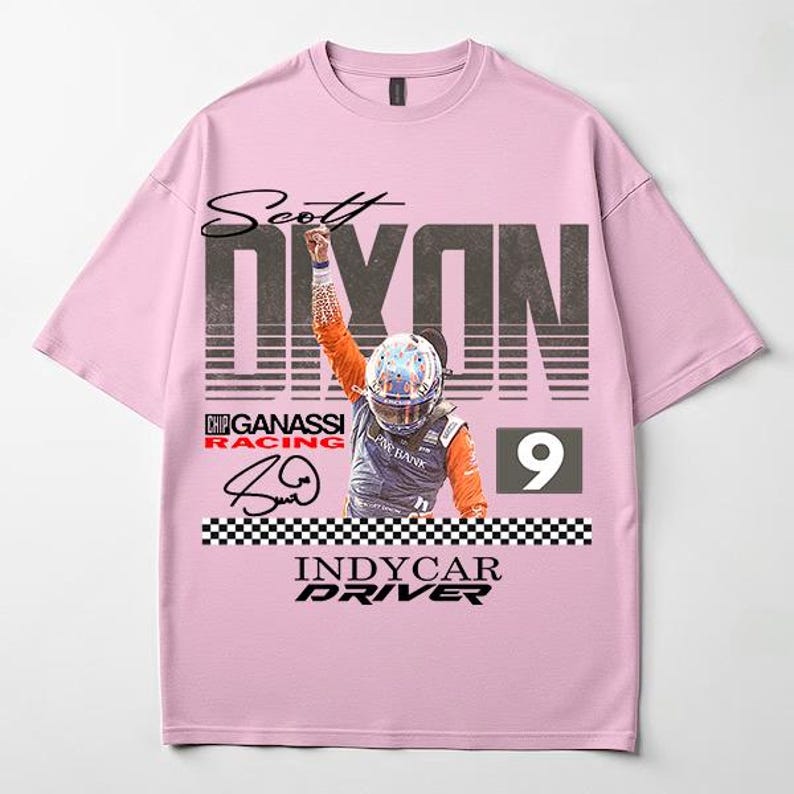 May include: A light pink t-shirt featuring a graphic of IndyCar driver Scott Dixon. The design includes the driver's name, the number 9, and the words "INDYCAR DRIVER". The shirt also features a checkered flag design.