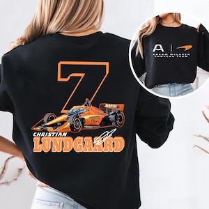 May include: Black sweatshirt with an orange number 7, a race car graphic, and the text "Christian Lundgaard" on the back. The front of the sweatshirt has the text "Arrow McLaren IndyCar Team" in white.