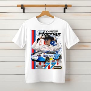 May include: White t-shirt featuring a graphic of a race car and a driver. The design includes the text "Carson Hocevar" and "77" along with the NASCAR Cup Series logo. The car is blue and white.