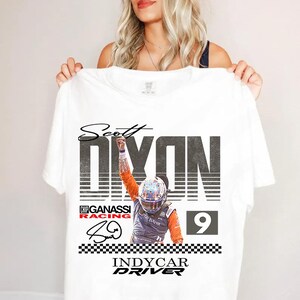 May include: White t-shirt featuring a graphic of Scott Dixon, an IndyCar driver, with the text "Scott Dixon" above a large "DIXON" and the number "9". The shirt also includes the text "Chip Ganassi Racing" and "IndyCar Driver".