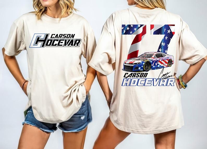 Op de afbeelding: Beige T-shirt met de naam "CARSON HOCEVAR" in zwarte en blauwe letters op de voorkant. De achterkant toont het nummer "77" met een Amerikaans vlagontwerp en een raceauto-afbeelding. Het shirt heeft een casual, oversized pasvorm.