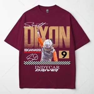 May include: Maroon t-shirt featuring a graphic of IndyCar driver Scott Dixon. The design includes his name, signature, racing team logo, and the number 9. The shirt has a crew neck and short sleeves.