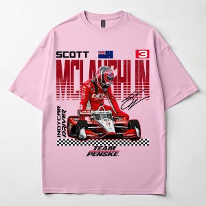 May include: Pink t-shirt featuring a graphic of an IndyCar driver in a red racing suit and helmet, with a race car. The text includes "SCOTT MCLAUGHLIN", "INDYCAR DRIVER", and "TEAM PENSKE".