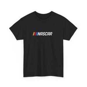 May include: Black t-shirt featuring the NASCAR logo. The logo includes three vertical stripes in red, yellow, and blue, followed by the word "NASCAR" in white. The shirt is a classic crew neck style.