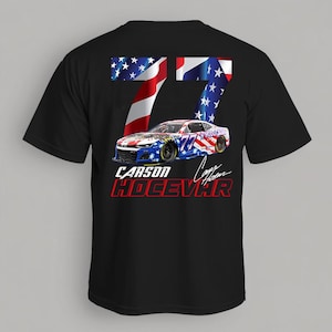 Op de afbeelding: Zwart T-shirt met een afbeelding van een raceauto, nummer 77 en een ontwerp van de Amerikaanse vlag. Het shirt toont ook de naam "Carson Hocevar" in rode en witte tekst.