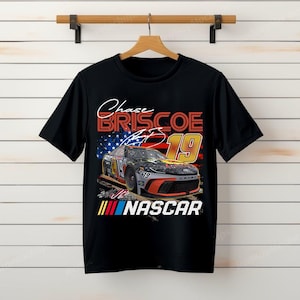 May include: Black t-shirt featuring a graphic of a race car with the number 19 and the name "Chase Briscoe." The design includes the American flag and the word "NASCAR."
