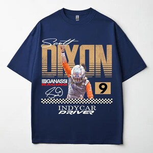 May include: Navy blue t-shirt featuring a graphic of a race car driver with the name "Scott Dixon" and the word "Dixon" in large, distressed gold letters. The number "9" is also visible. The shirt includes the text "Indycar Driver".