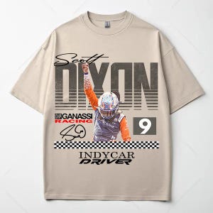 May include: Beige t-shirt featuring a graphic of IndyCar driver Scott Dixon. The design includes the driver's name, racing team logo, signature, and the number 9. The shirt has a crew neck and short sleeves.