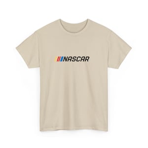 May include: A beige t-shirt featuring the word "NASCAR" in black, with a colorful stripe design above the text. The shirt is a short-sleeved crew neck style.