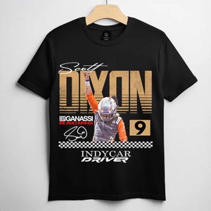 May include: Black t-shirt featuring a graphic of IndyCar driver Scott Dixon. The design includes the driver's name, a racing helmet, the number 9, and the words "INDYCAR DRIVER". The shirt has a checkered flag design at the bottom.