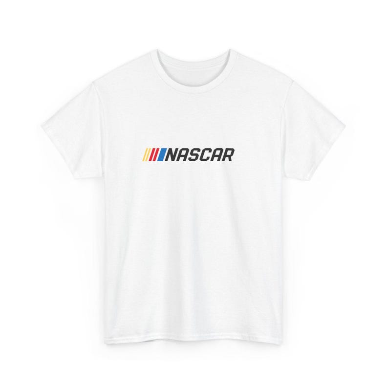 May include: White t-shirt featuring the word "NASCAR" in black, with a colorful stripe design above the text. The stripes are yellow, red, and blue. The shirt is a crew neck style.