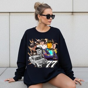 May include: A navy blue sweatshirt featuring a collage of race car drivers and a race car. The number "77" is prominently displayed. The design includes lightning bolt graphics and various portraits of the drivers.