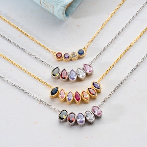 May include: Four gold necklaces with teardrop-shaped gemstones. The necklaces feature different colored gemstones, including red, blue, purple, and clear.
