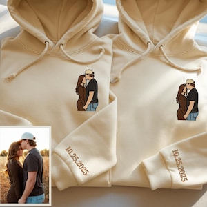 May include: Two beige hoodies with matching embroidered couple illustrations and the date "10.25.2025" on the sleeves. Each hoodie features a drawstring hood and a front pocket. A small photo of the couple is in the lower left corner.