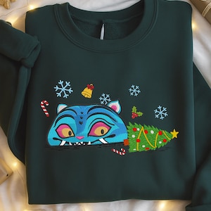 May include: Dark green sweatshirt featuring a blue cat-like creature with yellow eyes, a Christmas tree, snowflakes, and candy canes. The design is embroidered. A cozy, festive garment.