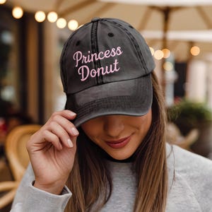 May include: A black baseball cap with a pink embroidered design that says "Princess Donut".