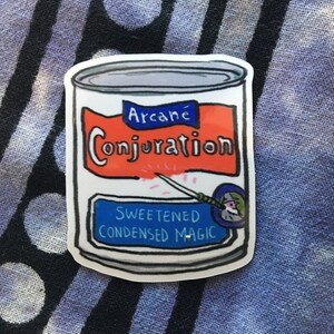 May include: A sticker featuring a cartoon can of "Arcane Conjuration Sweetened Condensed Magic." The can is white with a gray lid and orange label. A blue banner reads "Sweetened Condensed Magic."