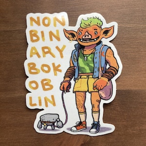 Peut inclure: Autocollant représentant un gobelin orange aux cheveux verts et un gilet bleu, marchant avec une petite créature grise et carrée en laisse. L'autocollant porte les mots "NON BINARY BOK OB LIN" en jaune. Le gobelin porte un short jaune et des baskets oranges.