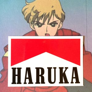 Puede incluir: Una pegatina con un diseño rojo y blanco y la palabra "HARUKA" en letras negras en negrita. La pegatina está colocada sobre un fondo de un personaje de anime con pelo rubio y un atuendo rojo.