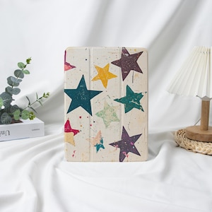 Könnte beinhalten: Eine cremefarbene Tablet-Hülle mit einem bunten Sternmuster. Die Sterne sind in verschiedenen Farben, darunter Blau, Gelb, Grün und Lila, mit einem Used-Look im Vintage-Stil. Die Hülle ist geschlossen und steht aufrecht.
