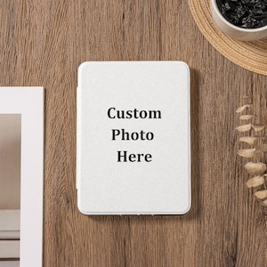 May include: A white rectangular item with rounded corners, featuring the text "Custom Photo Here" in black. The item is on a wooden surface, with a straw hat and a small bowl visible in the background.