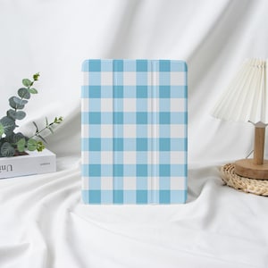 May include: A light blue and white checkered tablet case. The case is standing upright on a white surface. The case has a classic gingham pattern, with a light blue and white color scheme.