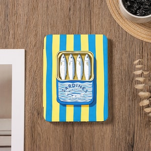 Könnte beinhalten: Ein rechteckiges Notizbuch mit blau-gelbem Streifenhintergrund. Es zeigt eine Illustration einer Sardinenbüchse mit vier Fischen. Die Dose ist mit "Sardines Wild Caught In Olive Oil" beschriftet.