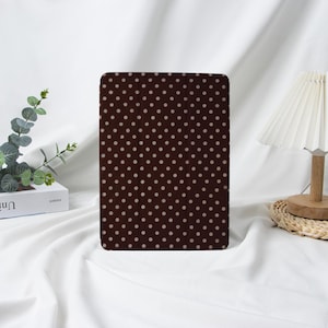 Op de afbeelding: Een donkerbruine tablethoes met een herhalend patroon van kleine, gelijkmatig verdeelde, lichtbeige stippen. De hoes is rechthoekig en lijkt gemaakt van een glad materiaal. De achtergrond is een witte stof.