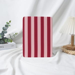 May include: A tablet case with a vertical striped pattern in shades of pink and red. The case is closed and appears to be made of a smooth material. The design is simple and modern.