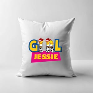 Peut inclure: Coussin carr&eacute; blanc avec le mot "GIRL" en lettres bleues et jaunes, le "I" &eacute;tant remplac&eacute; par une image de cowgirl de dessin anim&eacute;. Le mot "JESSIE" est imprim&eacute; en dessous sur un rectangle rose.