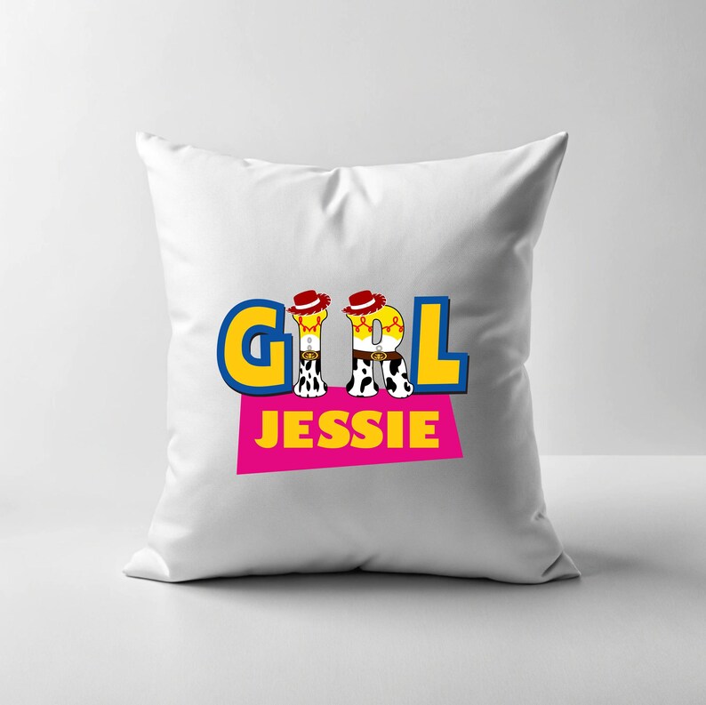 Peut inclure: Coussin carr&eacute; blanc avec le mot "GIRL" en lettres bleues et jaunes, le "I" &eacute;tant remplac&eacute; par une image de cowgirl de dessin anim&eacute;. Le mot "JESSIE" est imprim&eacute; en dessous sur un rectangle rose.